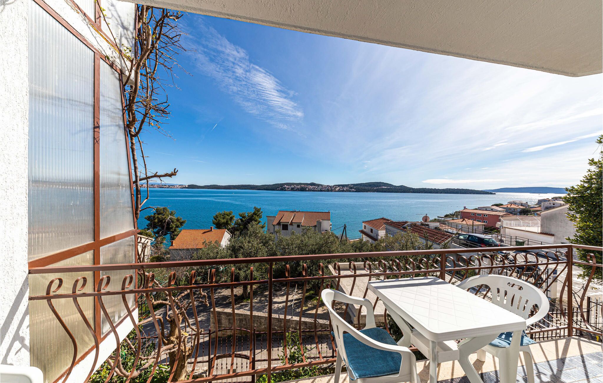 A balcony with a table and chairs, overlooking a coastal town and a body of water.