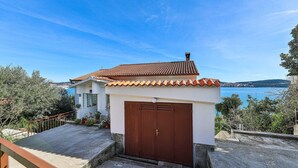 A coastal house with a tiled roof, a brown garage door, and a view of the sea. - Nice apartment in Seget Donji with house sea view (Seget Donji)