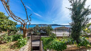 A stone gate leading to a garden with various plants and a view of the sea and distant hills. - Nice apartment in Seget Donji with house sea view (Seget Donji)