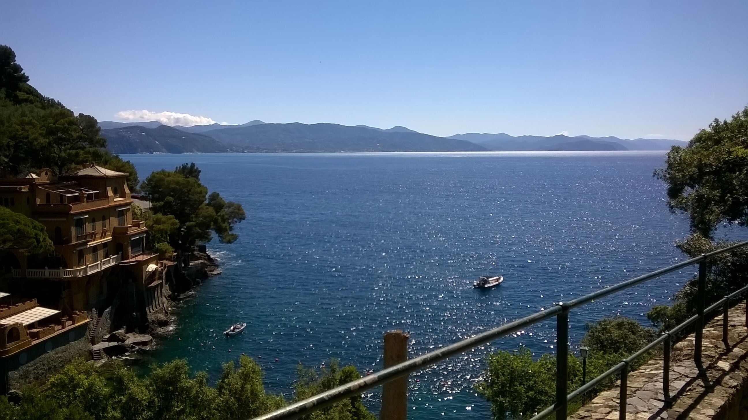 Vista costera con cielo despejado, un cuerpo de agua, barcos y un edificio con balcón que da al mar.