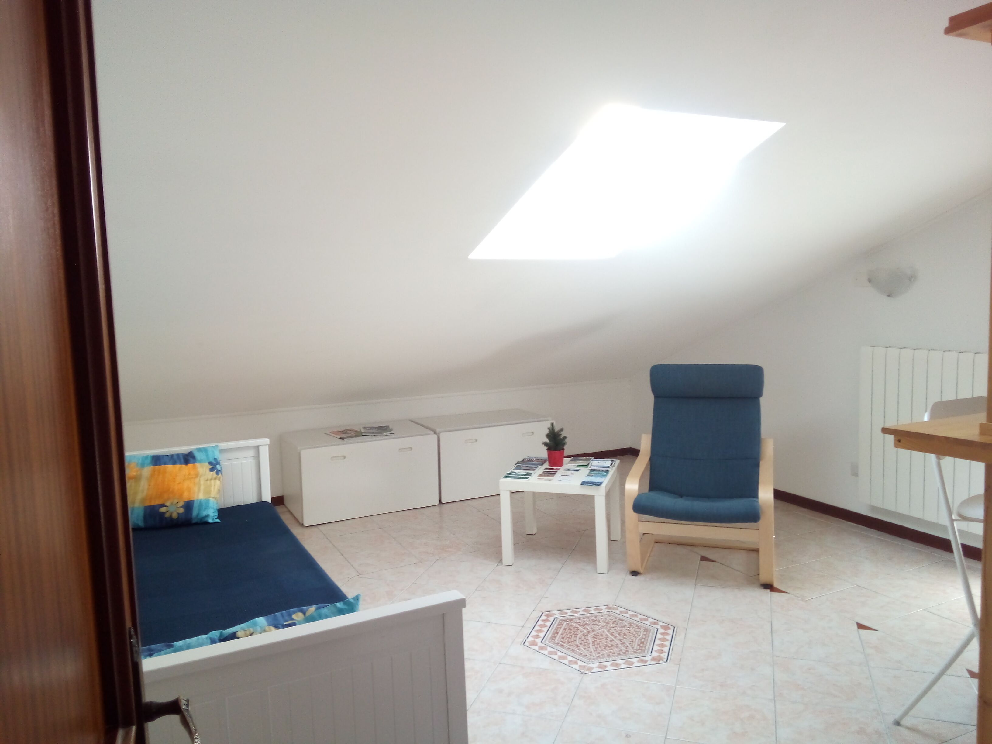 A small, tidy room with a bed, a chair, a table, and a radiator.