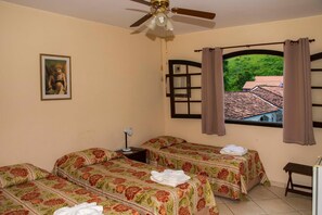 A room with two beds, a ceiling fan, a window with curtains, a painting on the wall, and a view of a house outside.
