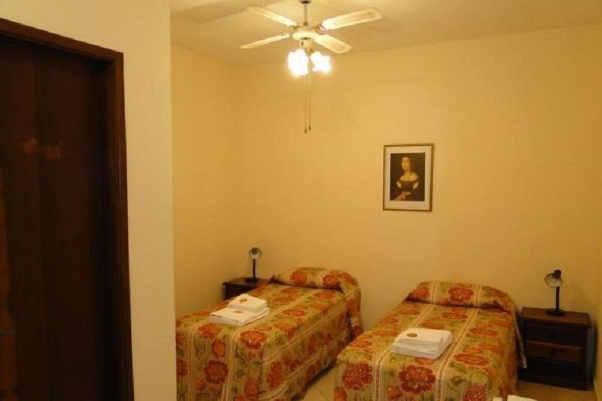 Une chambre avec deux lits, un ventilateur de plafond et une œuvre d’art encadrée au mur.