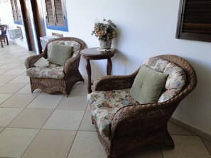 A room with two wicker armchairs with floral upholstery and a small round table with a vase of flowers.