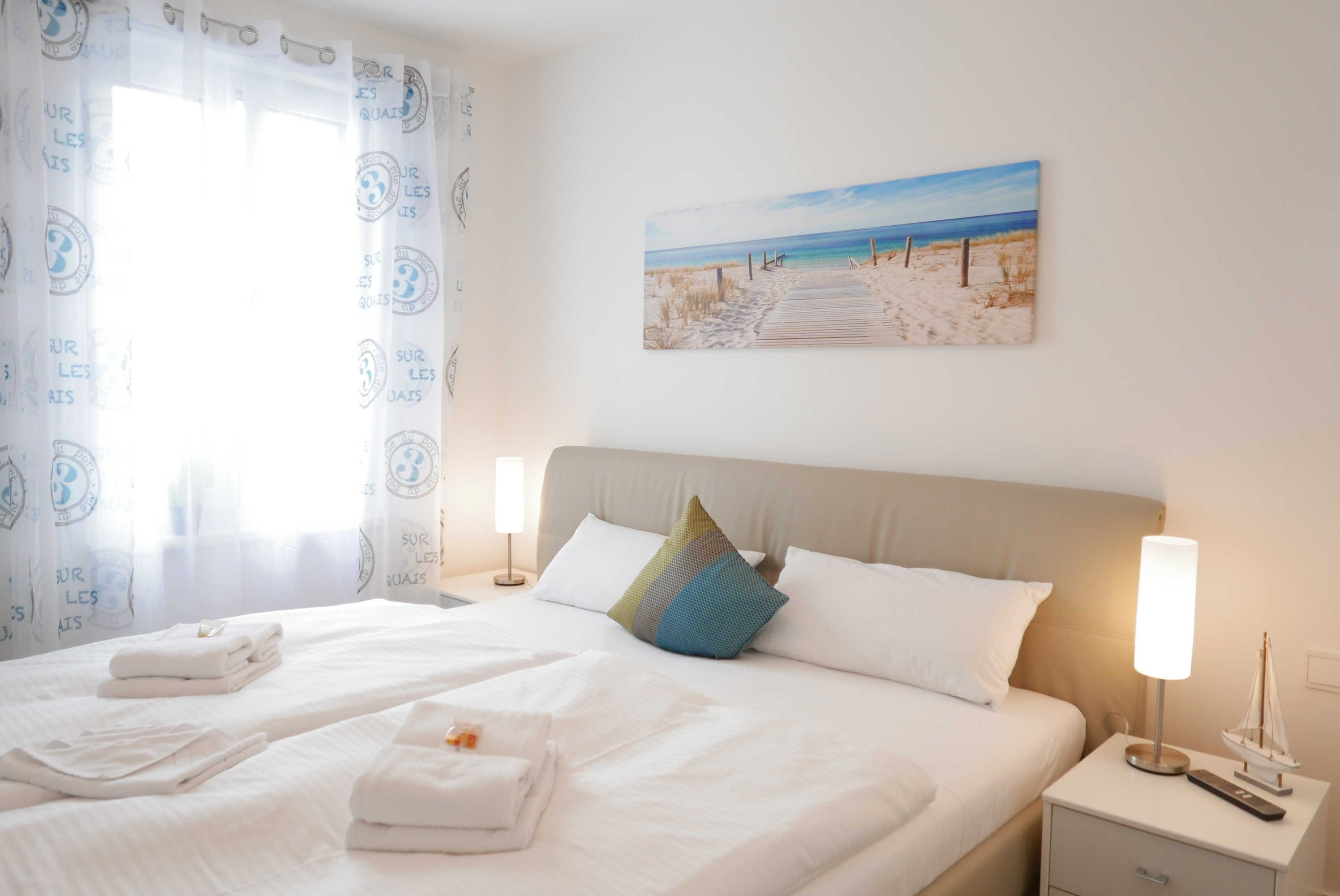 A neatly made bed with white linens, a pillow, and a bedside table with a lamp and a small decorative item.