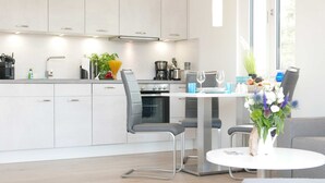A modern kitchen with white cabinets, a dining area with a table and chairs, and a large window providing natural light.