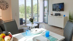 A dining area with a table set for two, a clock on the wall, and a TV mounted above the counter.