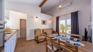 A compact living space with a kitchenette, two floral-patterned sofas, a dining table set for four, and a large window with curtains. - Gorgeous apartment in Smrika with WiFi (Smrika)