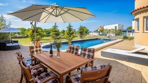 A wooden table with chairs and an umbrella in a backyard with a swimming pool and a view of the neighborhood. - Gorgeous apartment in Smrika with WiFi (Smrika)
