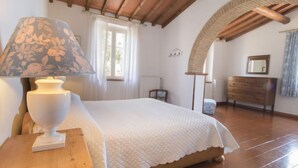 Un dormitorio con cama, una mesita de noche de madera, una lámpara, un armario y un arco de entrada.