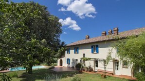 Una casa de dos pisos con techo de tejas, piscina y un jardín bien cuidado.