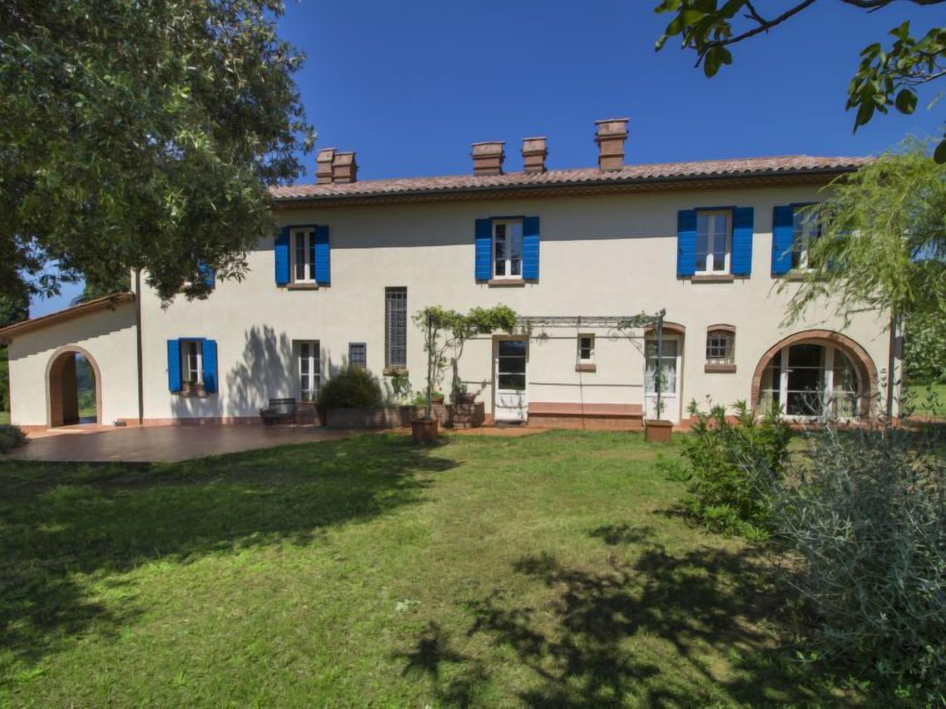 Un edificio a due piani con tetto in tegole, persiane blu e un piccolo giardino antistante.
