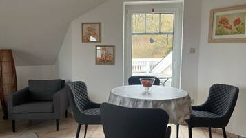 Un coin repas avec une table ronde, deux chaises, un vase de fleurs et une fenêtre donnant sur un balcon.