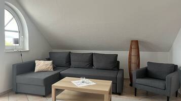 Un salon moderne avec un canapé d’angle gris, une table basse en bois et un grand lampadaire en bambou.