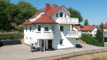 Une maison blanche à deux étages, avec un toit rouge, un balcon et une allée pavée.