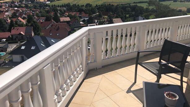 A balcony with a white balustrade, a table, a chair, and a potted plant.