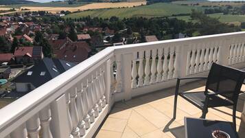Un balcon avec une balustrade blanche, une table, une chaise et un pot de fleurs.