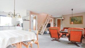 Une cuisine moderne avec des meubles blancs, un escalier en bois et un coin repas doté de chaises orange.