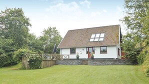Une maison de plain-pied avec un toit recouvert de tuiles, des murs extérieurs blancs et un petit porche à l’avant.