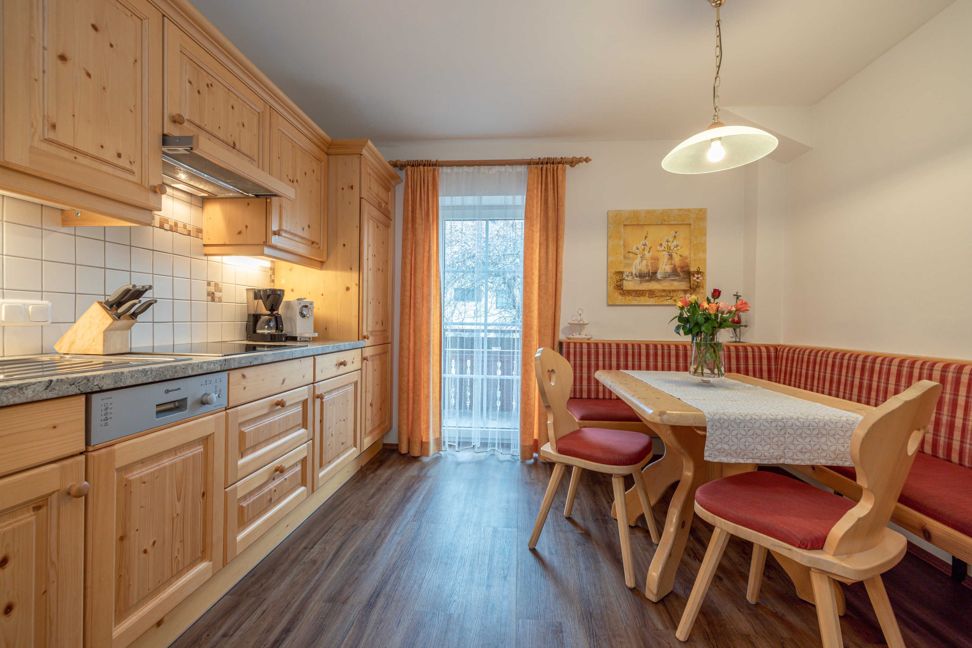 A kitchen with wooden cabinets, a dining table with chairs, a bench, and a hanging light fixture.