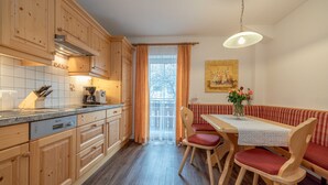 A kitchen with wooden cabinets, a dining table with chairs, a bench, and a hanging light fixture. - Apartment Dobratsch - Apartments Umfahrer Nassfeld (Tröpolach)
