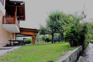 A residential building with a balcony, a wooden pergola, and a grassy yard.