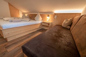 A room with a bed, a sofa, a wooden floor, and a wall-mounted light fixture. - Apartment Dobratsch - Apartments Umfahrer Nassfeld (Tröpolach)