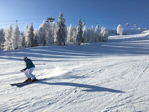 Une personne fait du ski sur une pente enneigée, sous un ciel dégagé, avec un télésiège en arrière-plan.