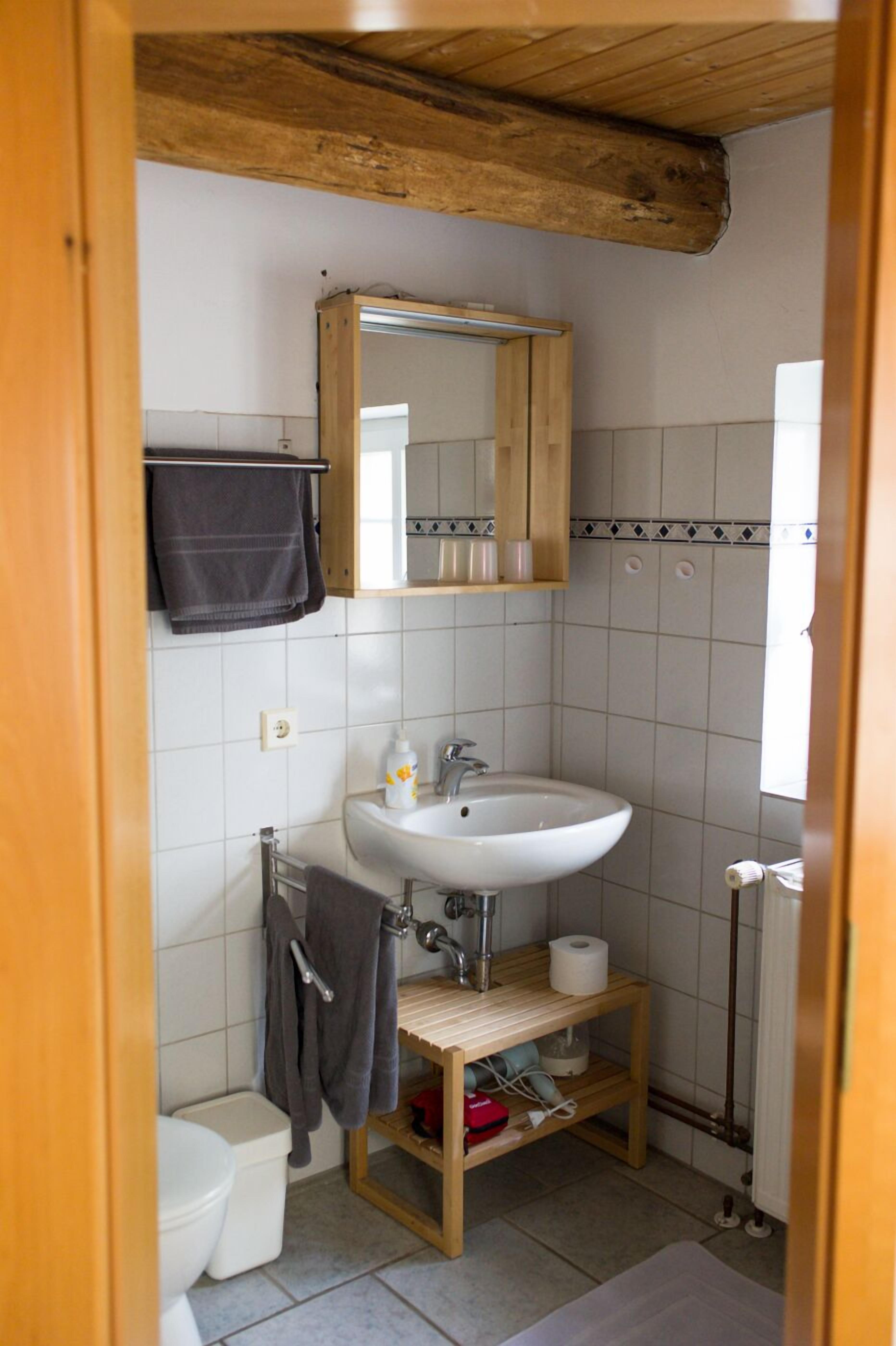 A small bathroom with a wooden vanity, a white sink, a mirror, and a towel rack.