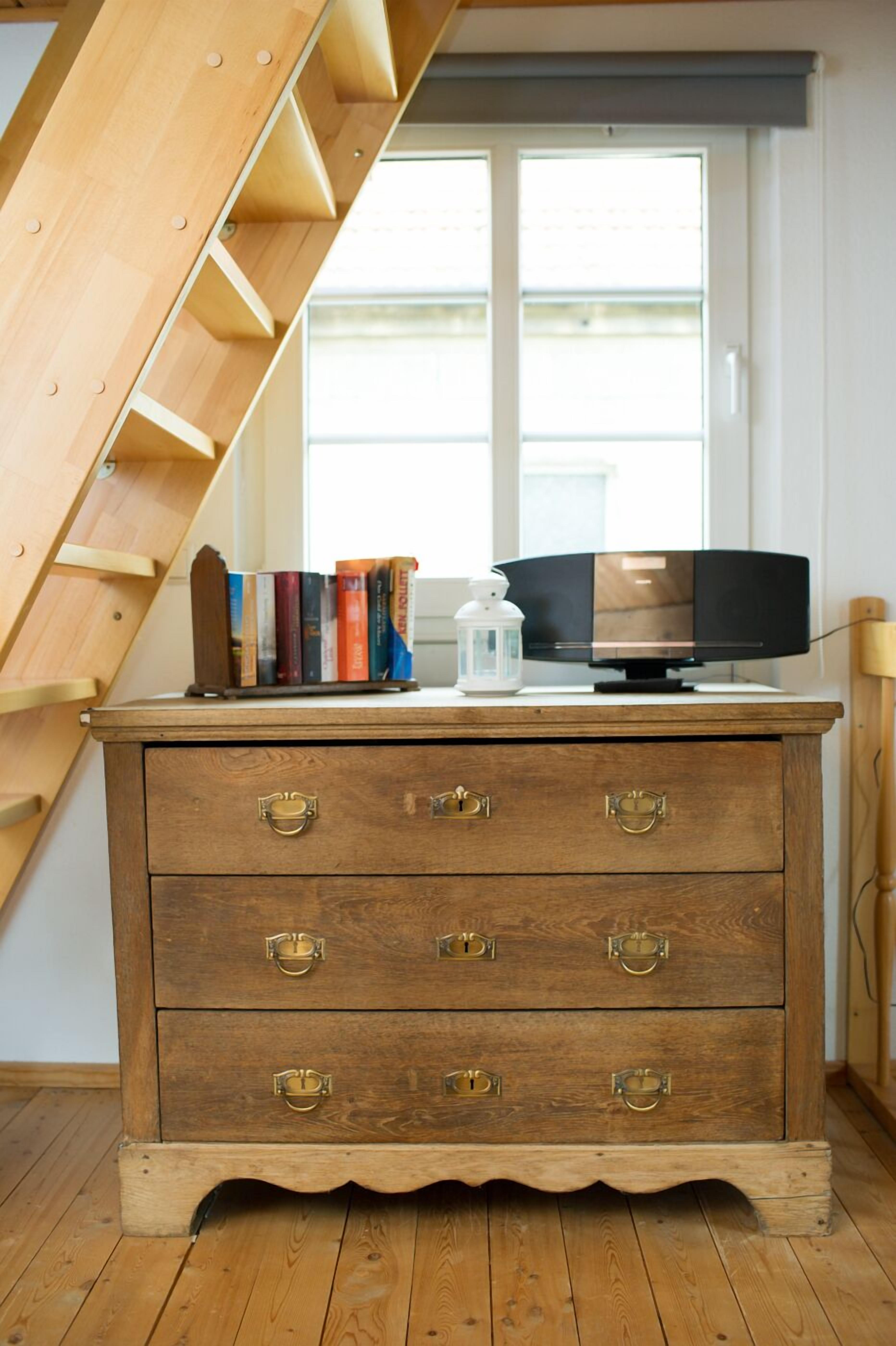 A wooden dresser with brass handles, a television, and books on top.