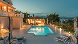 En pool med solstolar, en täckt uteplats och utsikt över det omgivande landskapet.