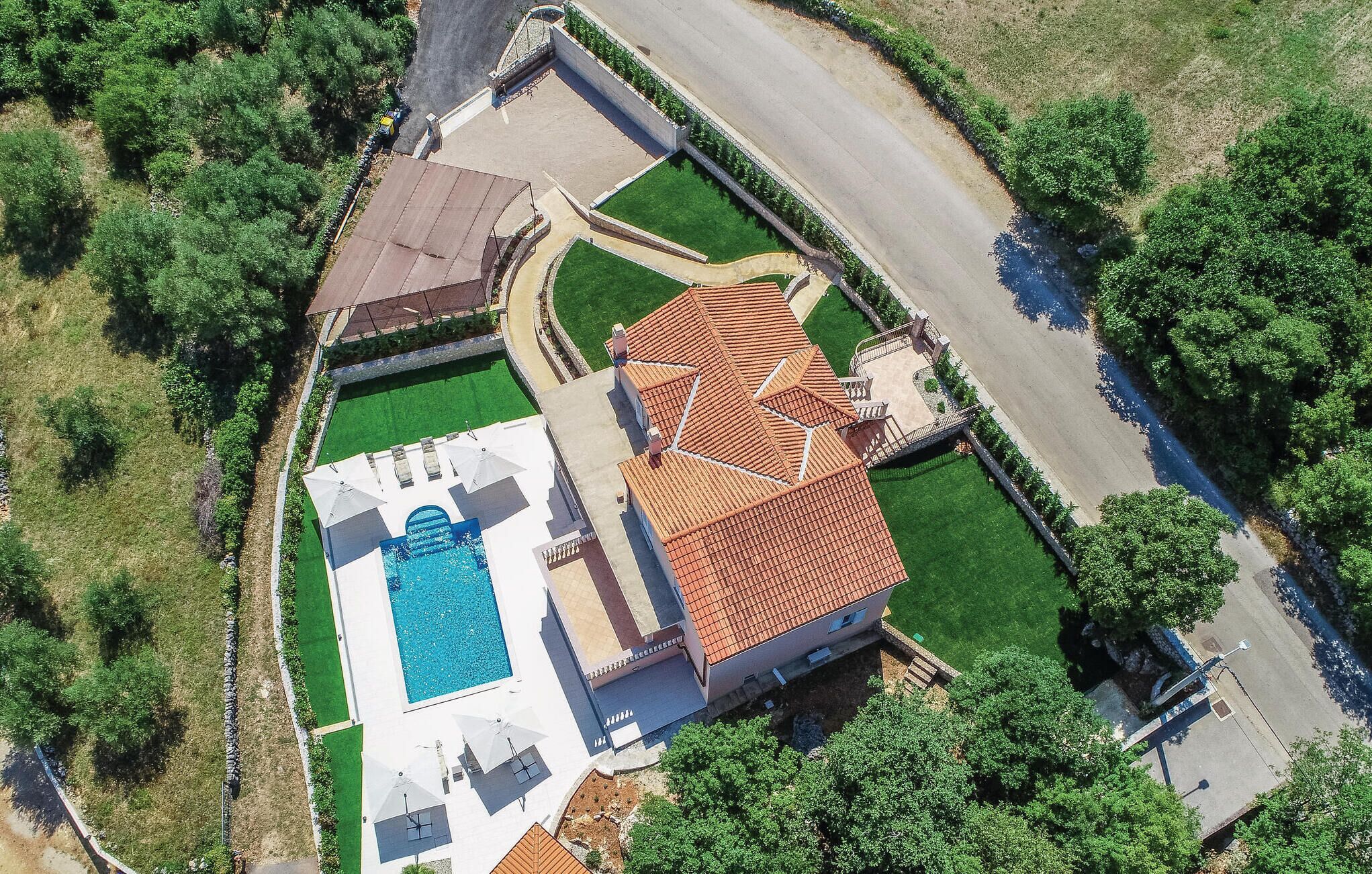 An aerial view of a property with a swimming pool, a covered patio, and a landscaped garden.