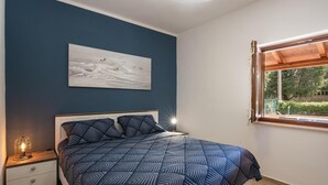 A bedroom with a bed, a nightstand, a lamp, a painting, and a window with a view of greenery. - Gorgeous home in Krnica (Krnica)