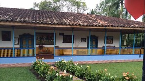 A building with a tiled roof, blue and yellow railings, and a garden with various plants. - Finca Hotel La Joya (Calarcá)
