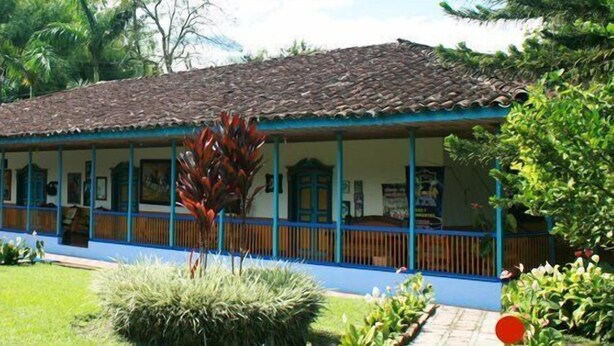 A building with a tiled roof and blue trim, surrounded by lush greenery. - Finca Hotel La Joya (Calarcá)