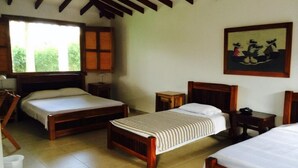 A room with two wooden beds, a small table, and a painting on the wall. - Finca Hotel La Joya (Calarcá)