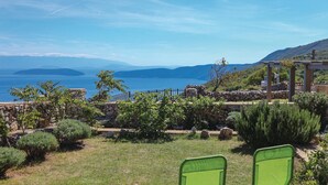 Vista costera con muro de piedra, sillas verdes y una pérgola con vista al mar.