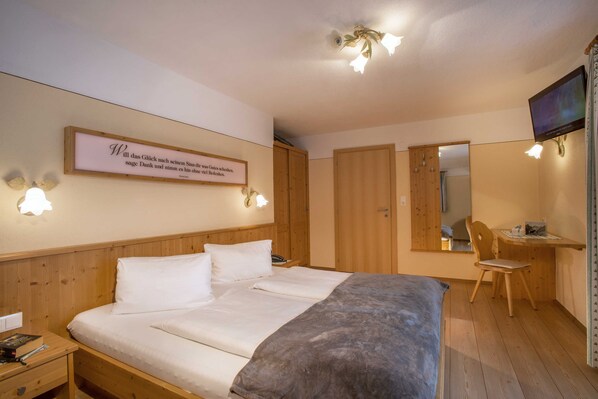 Une chambre à coucher comprenant un lit, une table de chevet, une lampe, un miroir et un téléviseur.