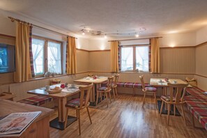 Un espace repas avec des tables et des bancs en bois, un téléviseur et des fenêtres avec des rideaux.