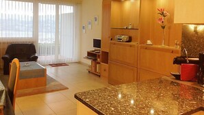 A modern living room with a dining area, a kitchen with wooden cabinets, and a large window with curtains. - Castagnola (Utoring) by Interhome (Castagnola)