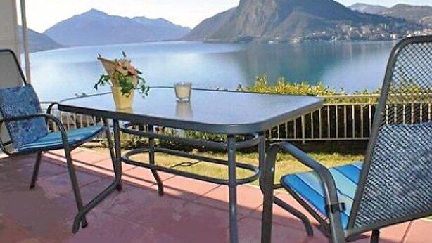 A patio with a table and chairs overlooking a lake and mountains. - Castagnola (Utoring) by Interhome (Castagnola)