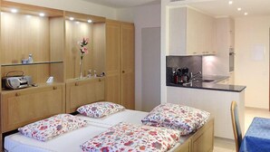 A bedroom with a bed, a small desk, and a kitchenette. - Castagnola (Utoring) by Interhome (Castagnola)