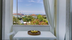 Una ventana con vistas a la costa, una mesa con una cesta de limones y una silla blanca.