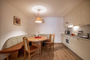 A compact kitchen with a round dining table, wooden chairs, a built-in oven, and a clock on the wall.
