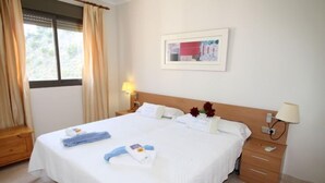 A hotel room with a large bed, two bedside tables, a window with curtains, a framed picture on the wall, and a lamp on the nightstand. - Torre Maestral by Interhome (Benidorm)