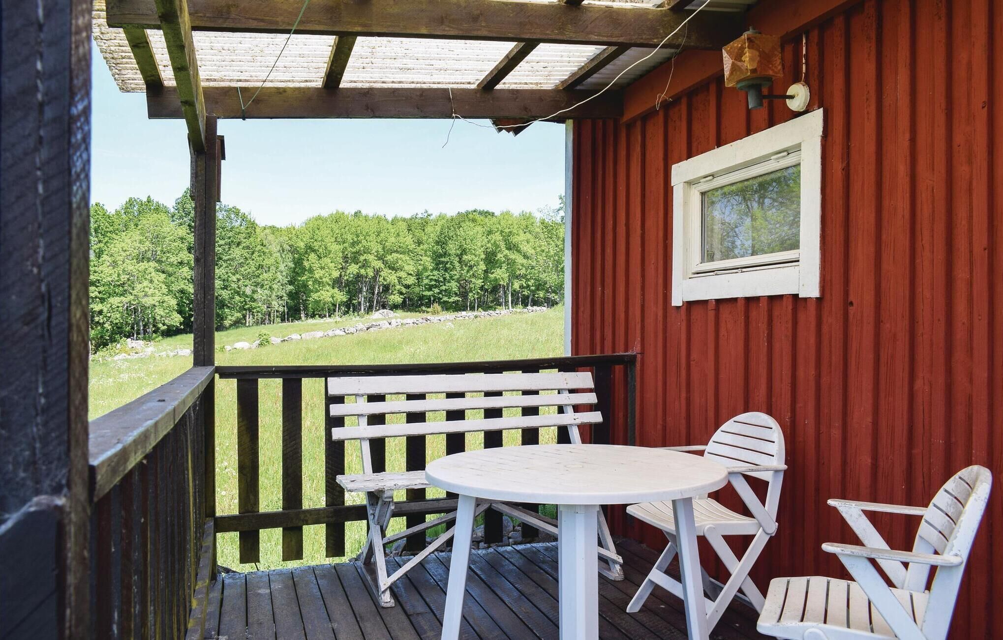 Eine Holzterrasse mit einem weißen Tisch und zwei weißen Stühlen, mit Blick auf eine grüne Wiese mit Bäumen.