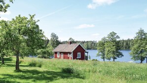 A red wooden house with a sloped roof, surrounded by lush green grass and trees, near a calm lake. - Awesome home in Ryd with house sea view (Ryd)