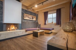 A cozy living room with a fireplace, a stone accent wall, a wooden bench, and a large window with curtains.
