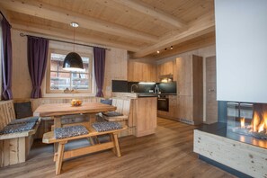 Un interior de madera con una mesa de comedor, bancos, una zona de cocina y una chimenea.