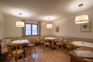 Un espace repas avec des tables et des chaises en bois, des luminaires suspendus et une fenêtre agrémentée de rideaux.
